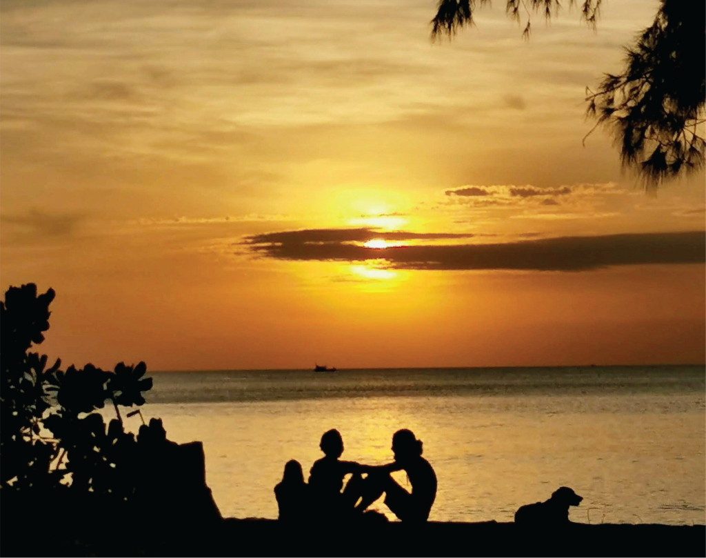 Silhouette of two people and a dog against the ocean sunset